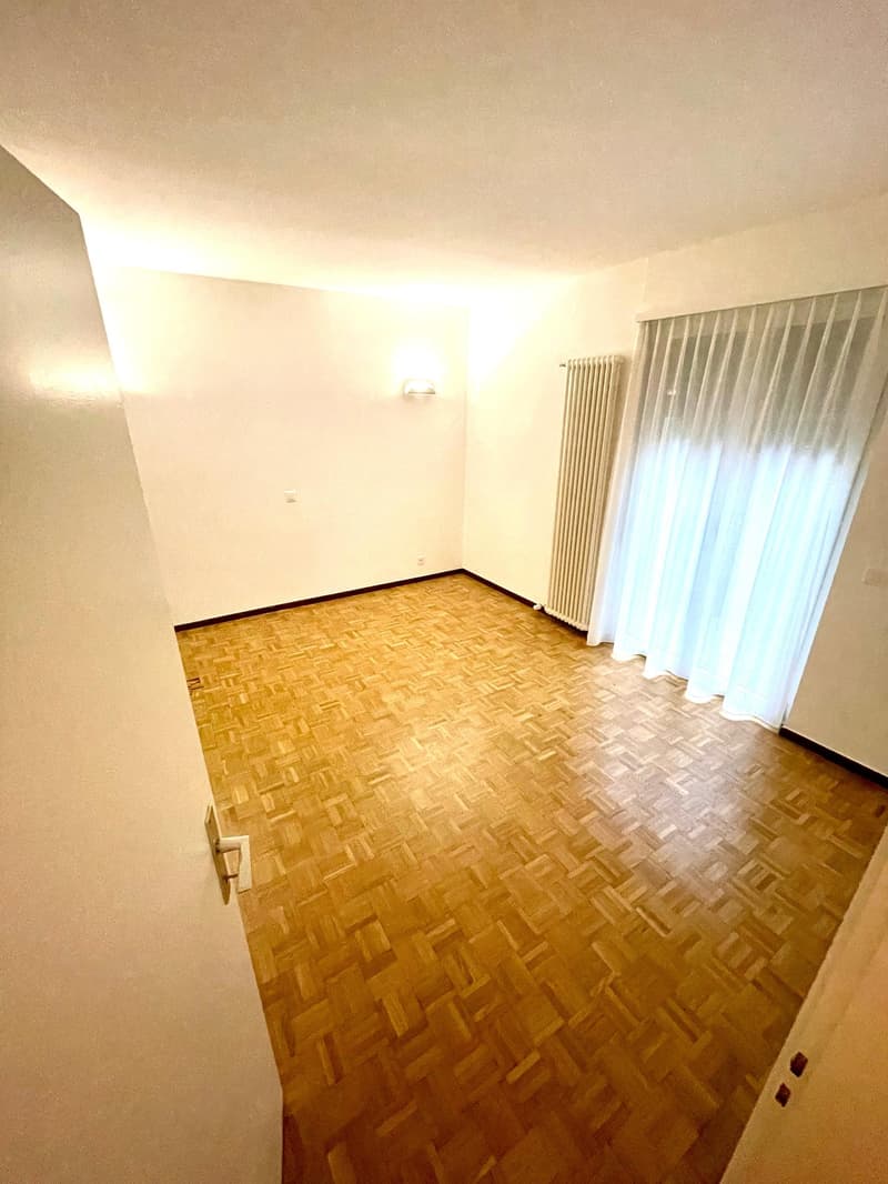 empty room with wooden floors, a radiator on the wall, white curtains