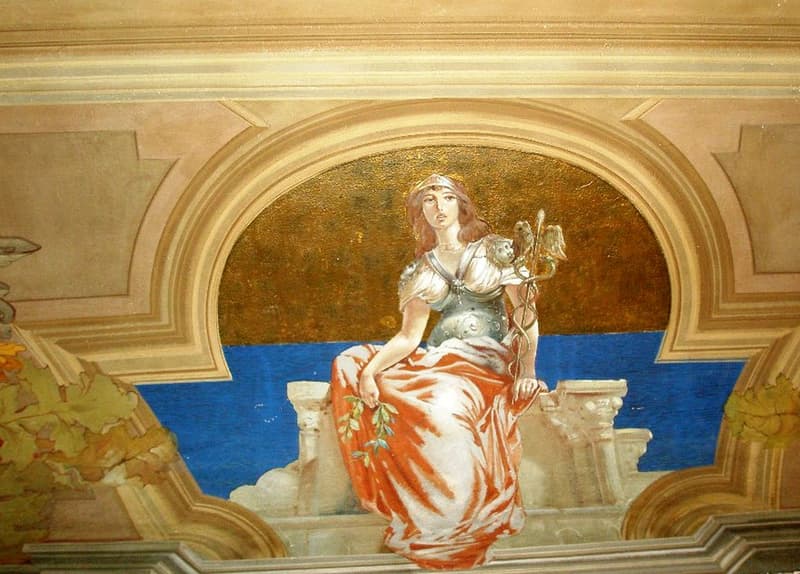 The image depicts a large, ornate painting featuring a female figure in a flowing, orange-red dress seated on a throne or pedestal. The figure has a crown or headdress and is holding a scepter or staff. The background is predominantly golden in color, wit
