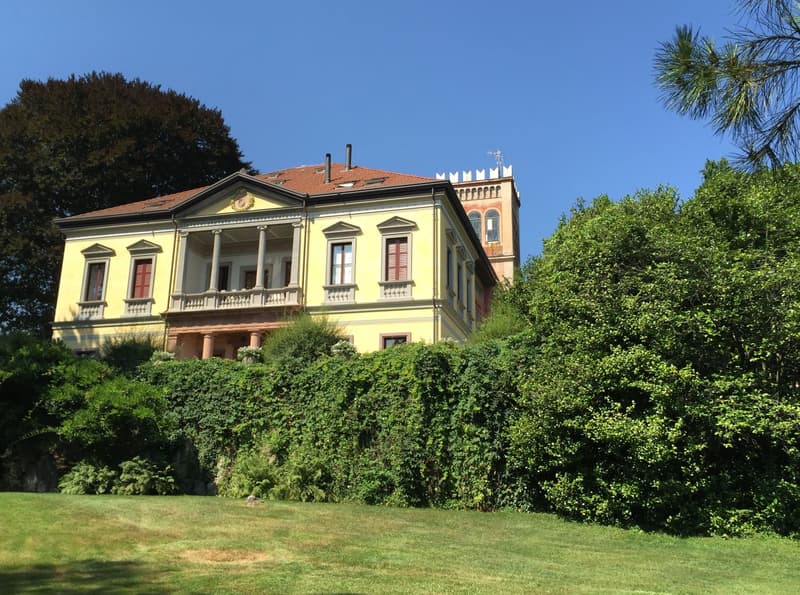 2-story yellow building with red tile roof, balconies, surrounded by lush greenery and trees