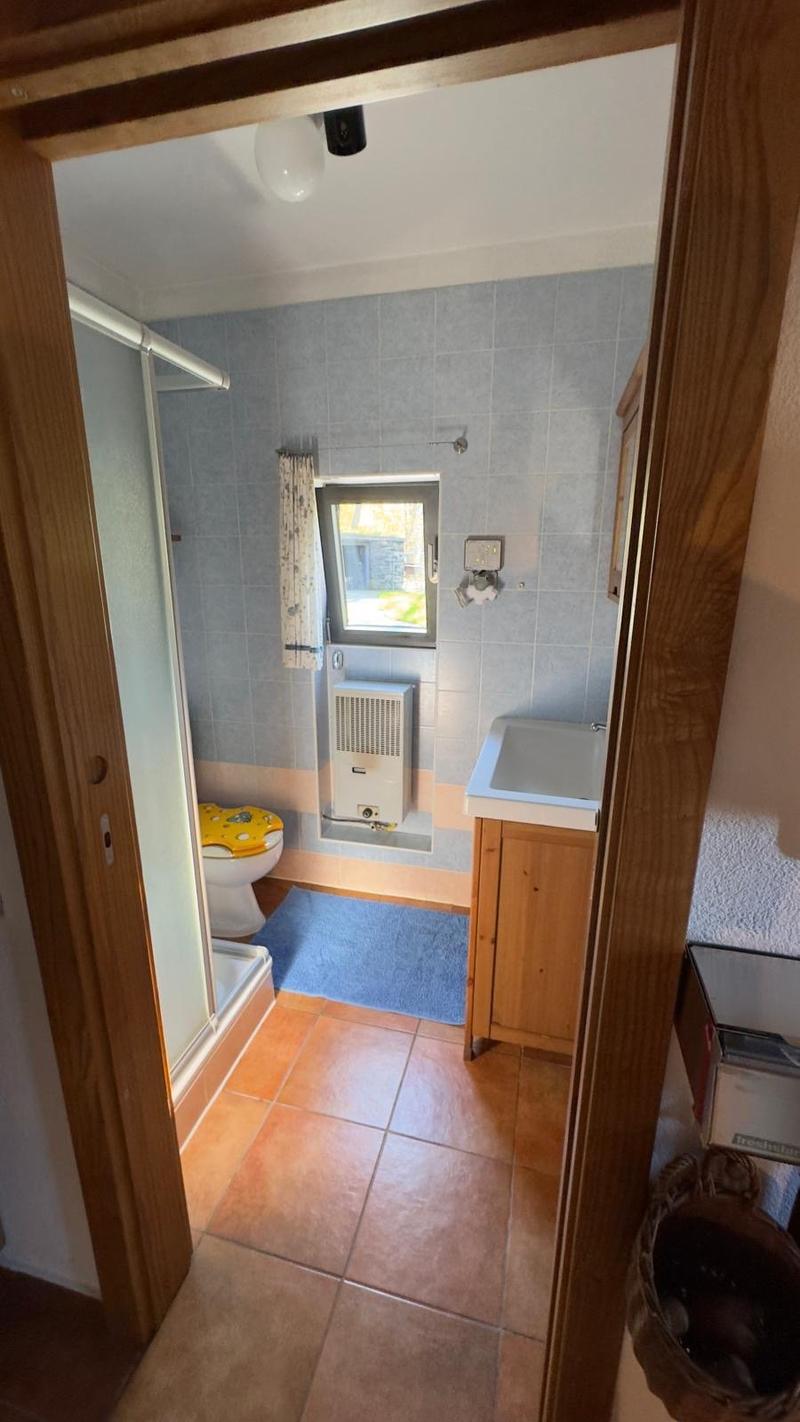 The bathroom features a shower stall, toilet, sink, blue tiled floor, a small window, and a heater below the window.