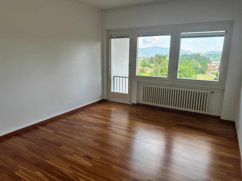 empty room with hardwood floors, white walls, large windows with view, glass door to balcony, white radiator
