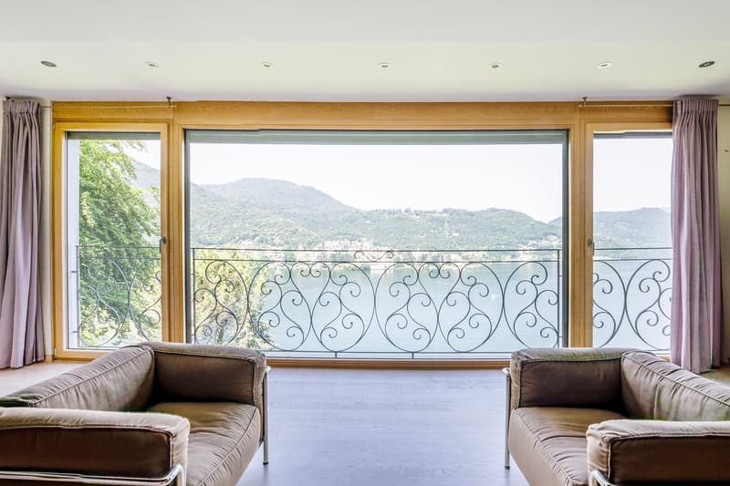 Large windows with a scenic mountain view, wooden frame, brown sofas, ornate metal railing on the balcony