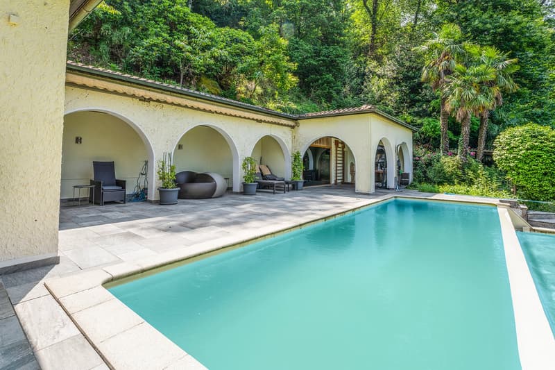 Outdoor patio with arched entryways, swimming pool, and lush greenery surrounding the property