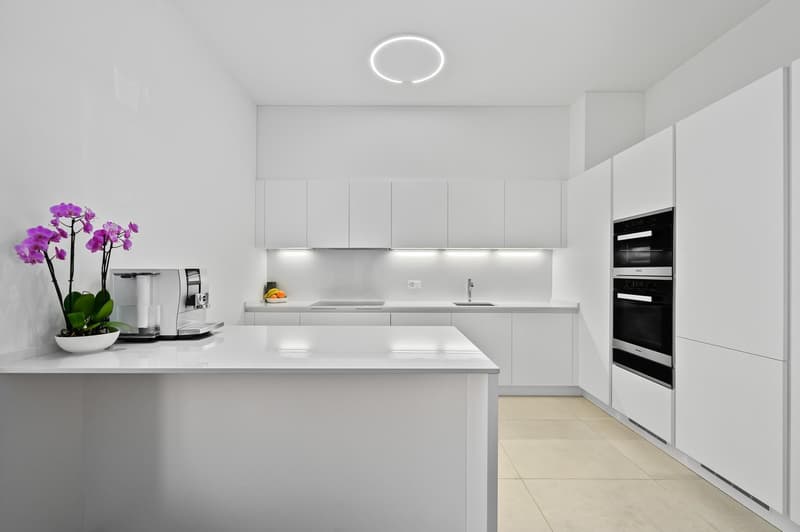 modern white kitchen with granite countertops, built-in ovens, sink with faucet, coffee machine, flowers, tile flooring