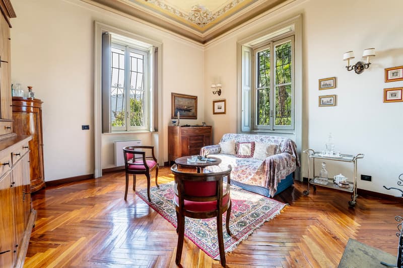 living room with hardwood floor, vintage wooden furniture, sofa, coffee table, wooden coffee cart, radiator, picture frames, windows