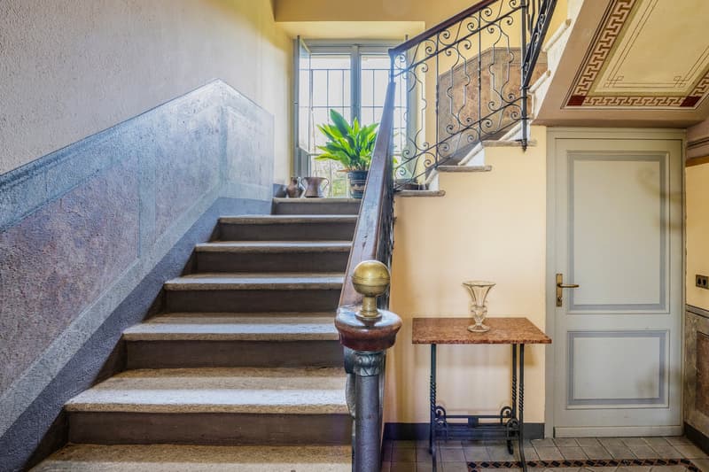 A large set of stairs leads to the entrance, a vase on the wall and some plant pots in the window