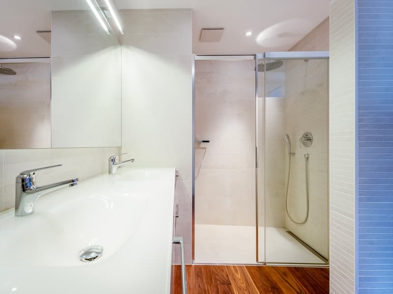 Modern bathroom with glass shower, white sink, white tiles, wooden floor