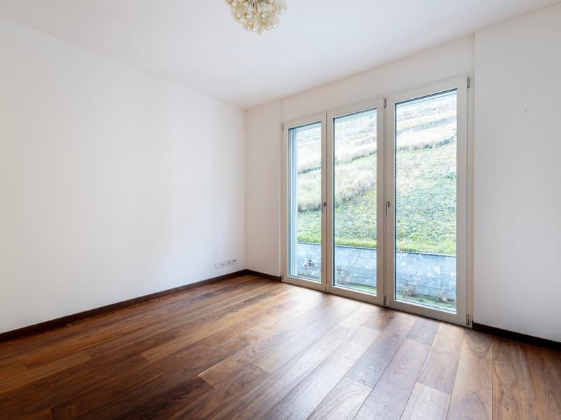 Empty room with wooden floor, white walls, sliding glass doors with outdoor view, modern chandelier