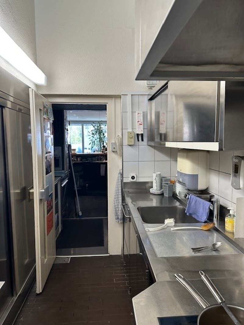 Commercial kitchen with stainless steel appliances, tiled floor, open door, sink, faucet, utensils, and a refrigerator.