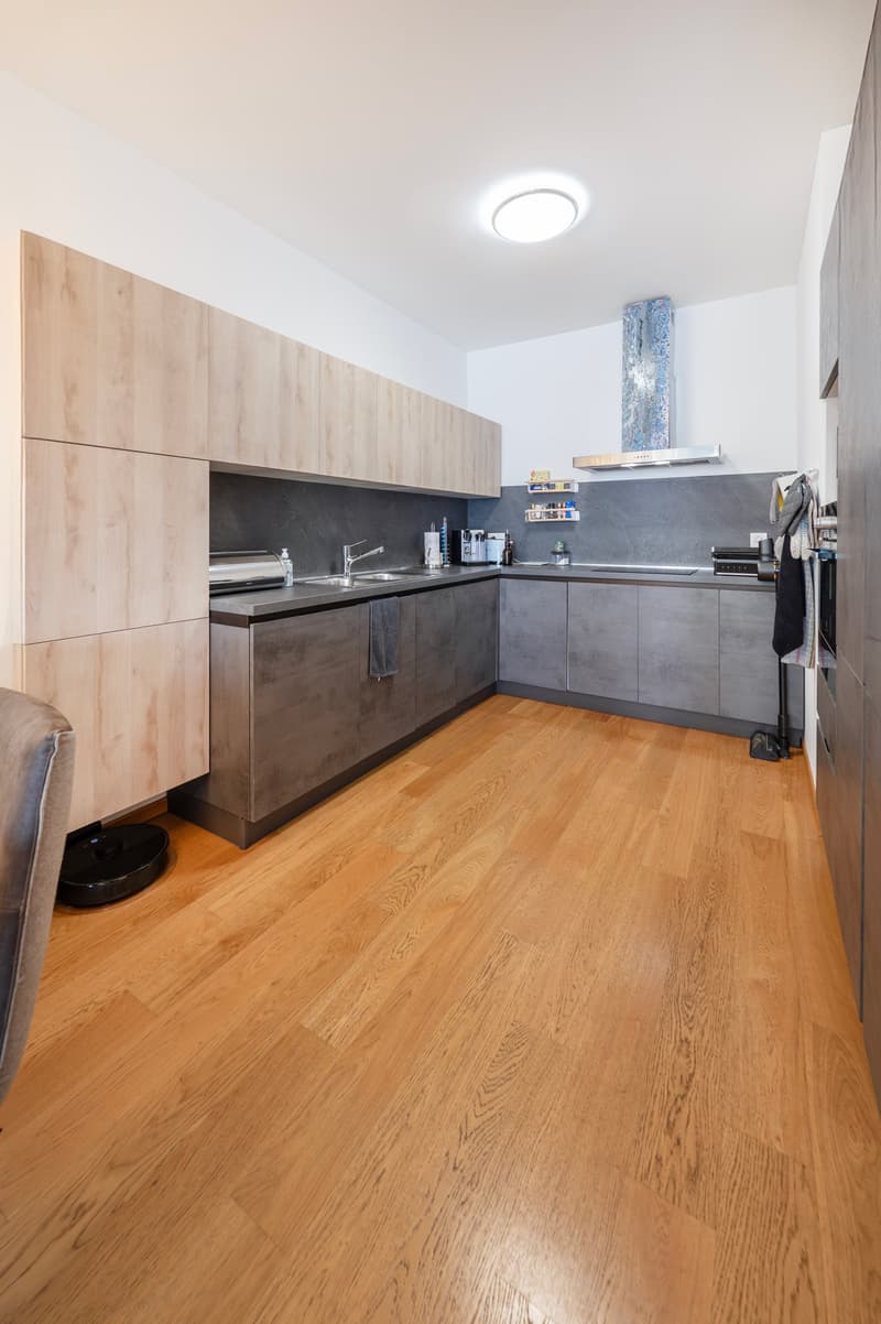Modern kitchen with wooden floors, stone countertop, stainless steel appliances, wooden cabinets, round ceiling light, open floor plan