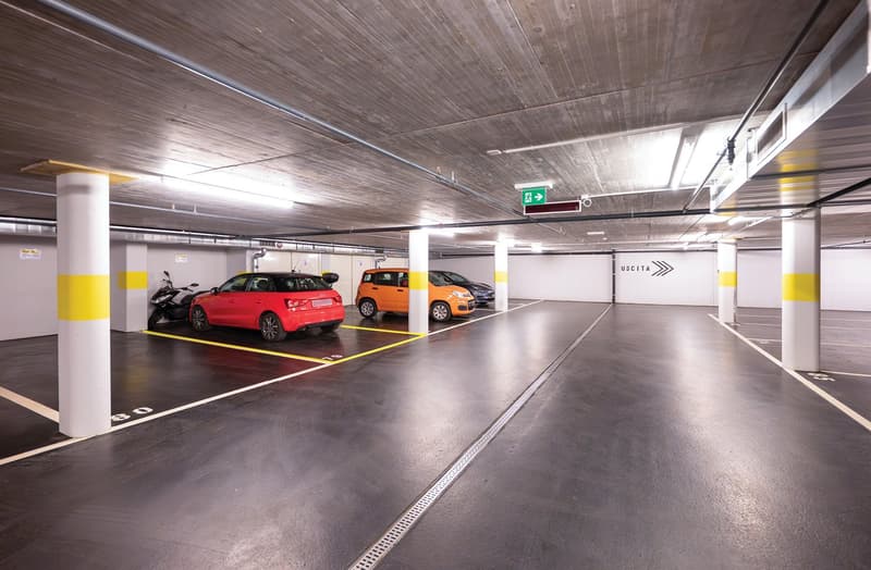 Underground parking lot with four parking spaces and one parking space for motorcycles, yellow and white painted pillars, parking lot is illuminated by fluorescent ceiling lights.