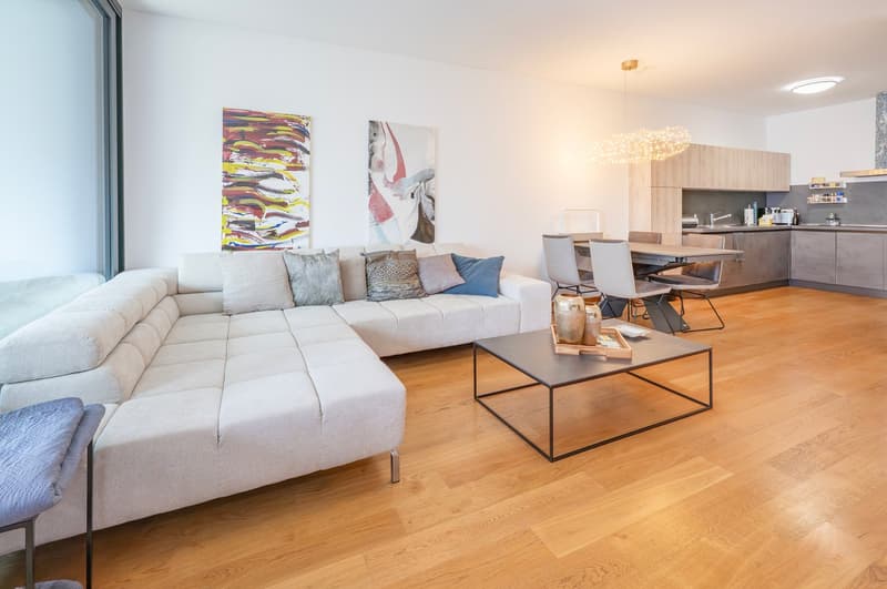 Living room with sectional sofa, wooden floor, large windows, chandelier, dining table, kitchen.