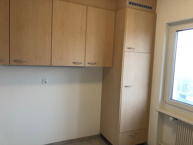 The image shows a kitchen area with wooden cabinets, a refrigerator, and a washing machine.
