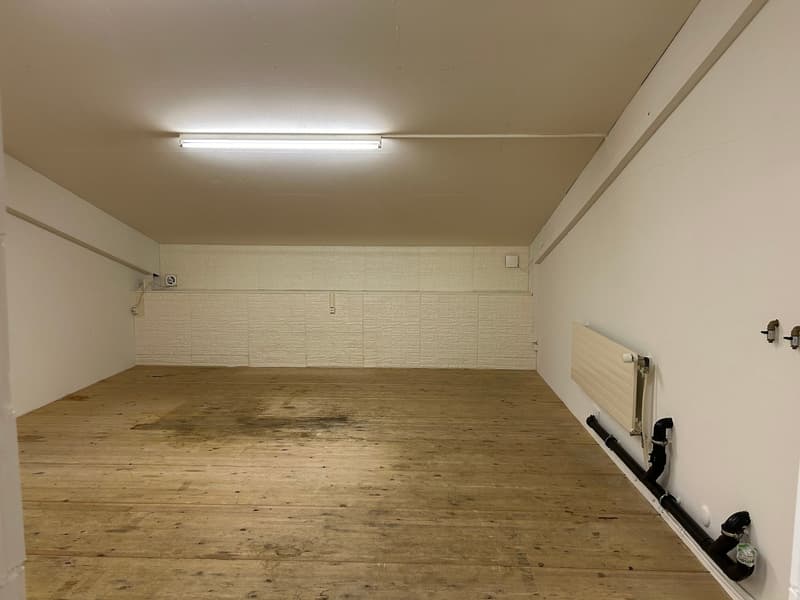 Empty room, wooden floor, white walls, radiator, lighting fixture on ceiling, black pipe on wall