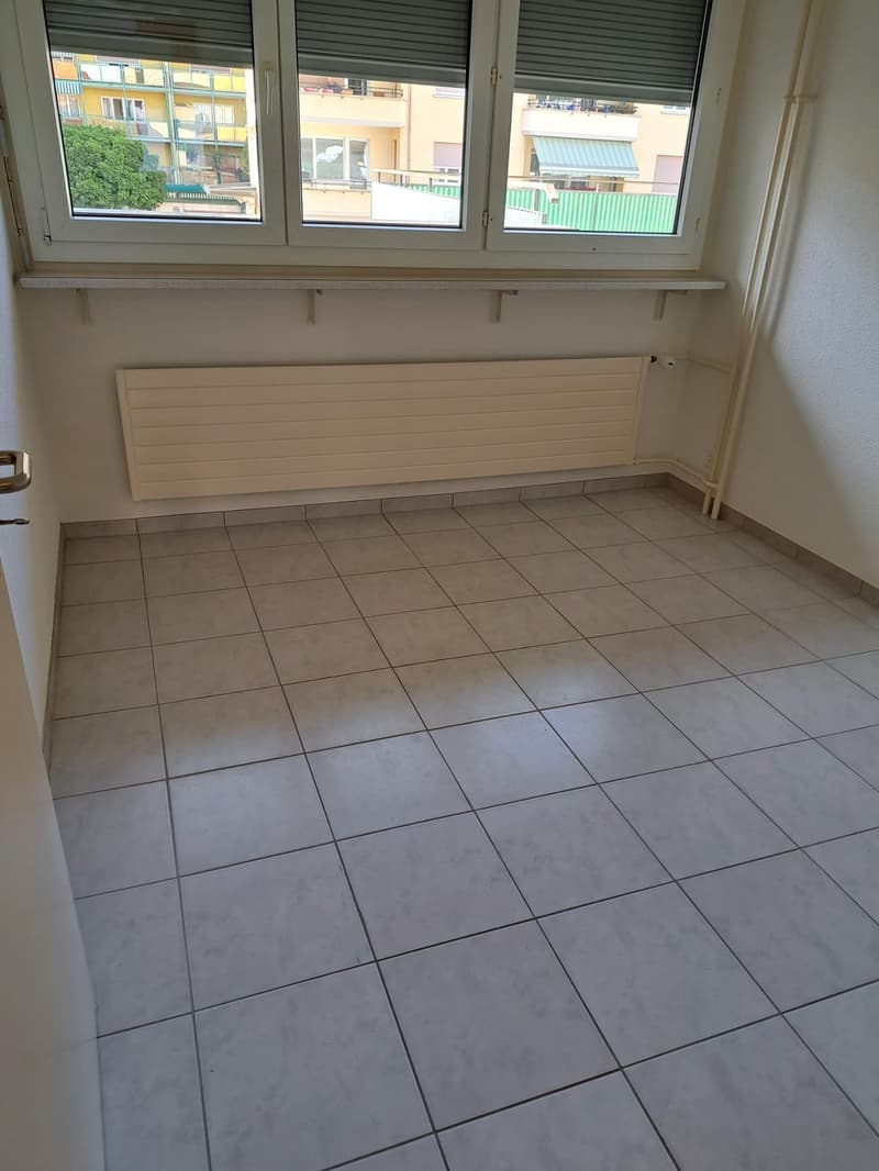 Empty room with large windows, radiator, tiled floor, bright daylight