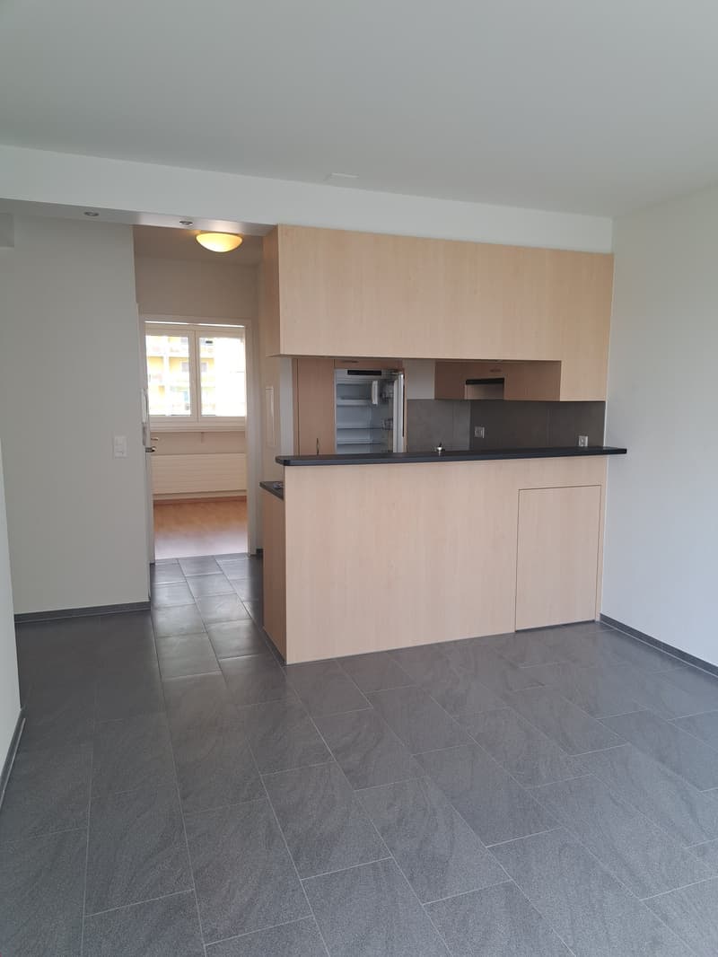 empty room with a modern kitchen with refrigerator and microwave, granite tiles flooring, white walls, an opening to another room