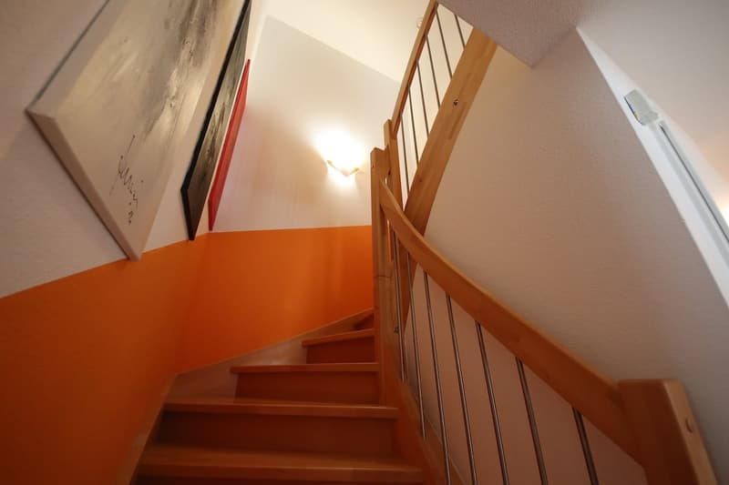 modern wooden staircase with railing, orange wall, light on the wall