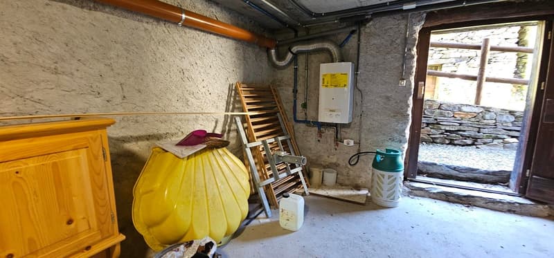 Storage room with a wooden cabinet, large yellow container, wooden ladder, two white buckets, metal cylinder, gas cylinder, gas boiler, pipes on the wall