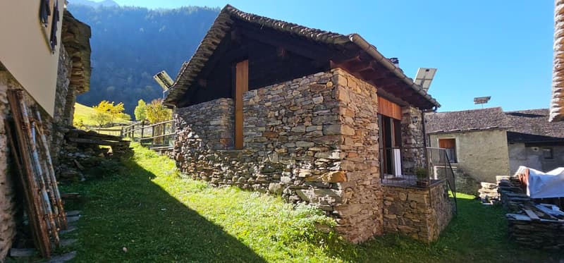 Raised ground floor, stone exterior, wooden doors, slanted roof, garden, mountains in the background