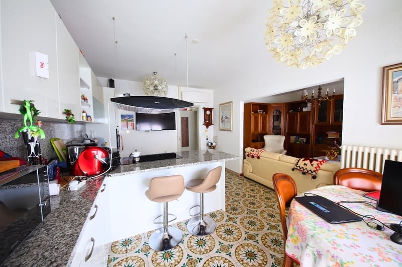 Counter with stools, dining table with laptop, couch, dining chairs, cabinet, picture frame, ceiling fan with chandelier