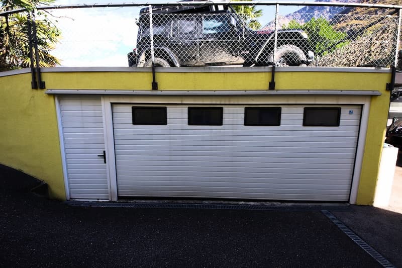 White garage door, fenced area on top, SUV parked above