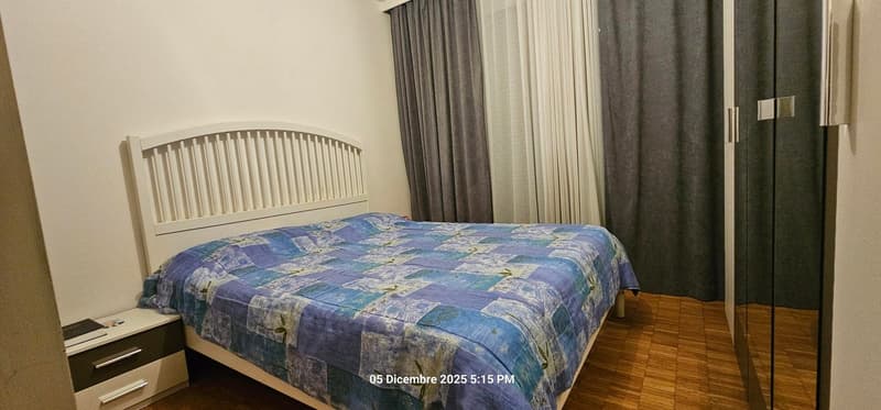 white walls, bed, nightstand, gray curtains