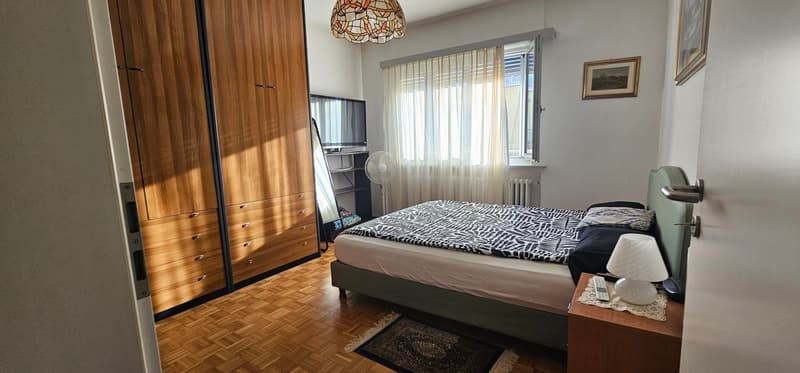 bedroom with wooden parquet flooring, bed, large wardrobe, TV on cabinet, table with lamp, curtains