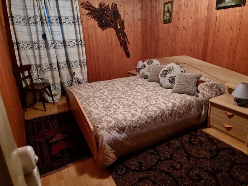 Master bedroom with wooden bed, wooden nightstands, white and black curtains, brown carpets, and a wooden chair.
