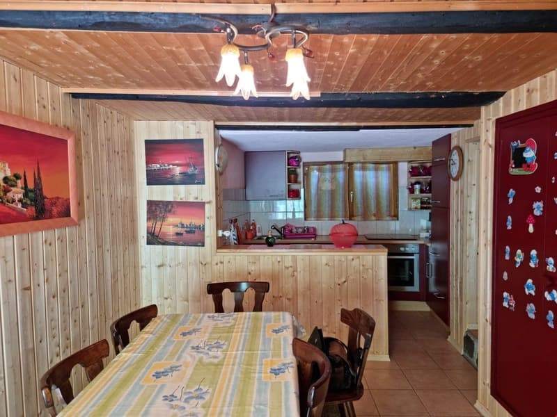 Dining area with table, chairs, and wooden paneled walls; open kitchen with dining counter and oven