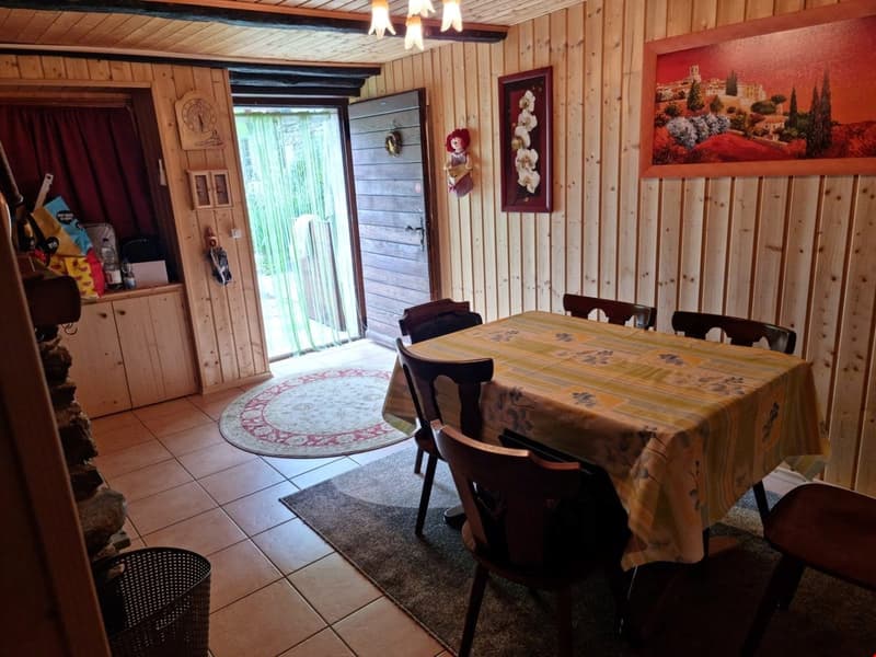 Wooden walls, dining table with chairs, rug, wooden cabinet, hanging decoration, framed paintings, shelves, open door, window, door