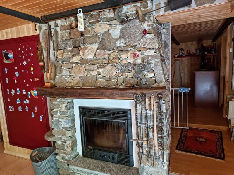 Rustic stone fireplace with a black firebox, a wooden mantel, and a metal tong stand, red door with decorations