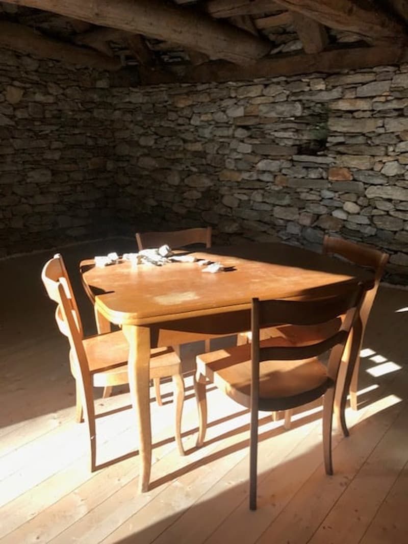 A room with a wooden table and chairs, stone wall, wooden ceiling