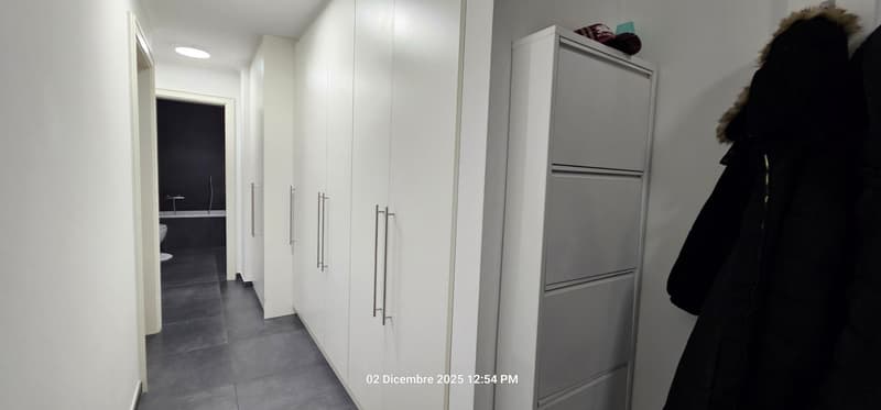 Empty hallway with large built-in wardrobes on one side, an open doorway to the bathroom in the background, and a coat rack on the right.