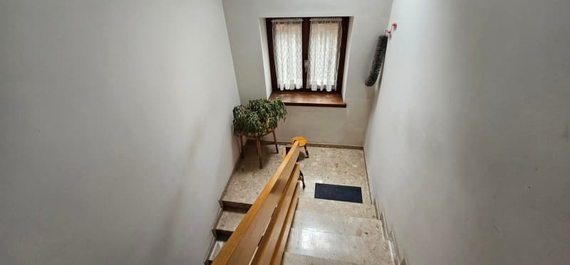 wooden staircase, white walls, white tiled floor, plant on wooden stand, window with white lace curtain, red wall mounted hook