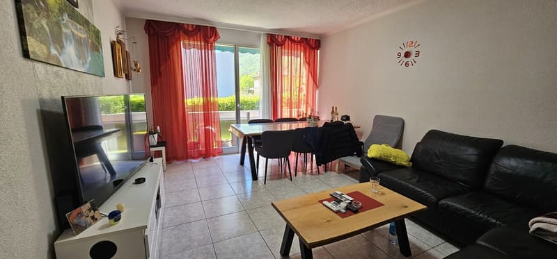 living room with sofa, coffee table, TV, dining table, chairs, balcony, curtains, wall clock, paintings, and a view of the outside