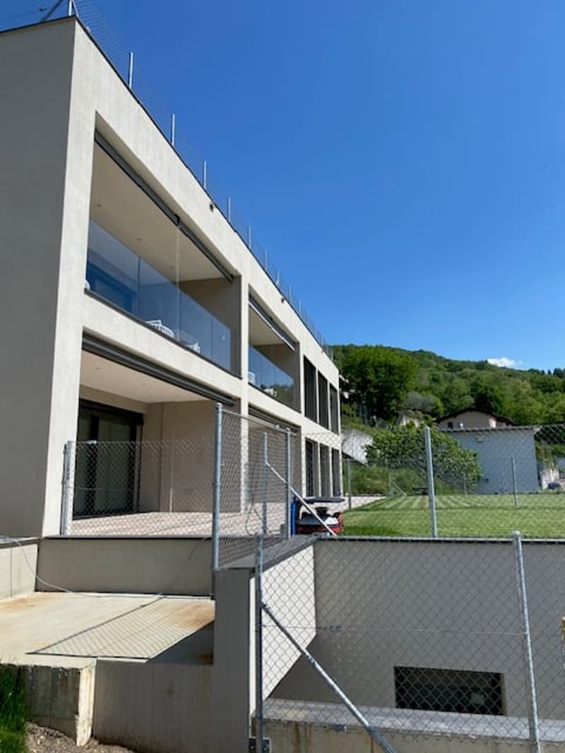 A modern multi-story building with large windows, balconies, and a fenced outdoor area.