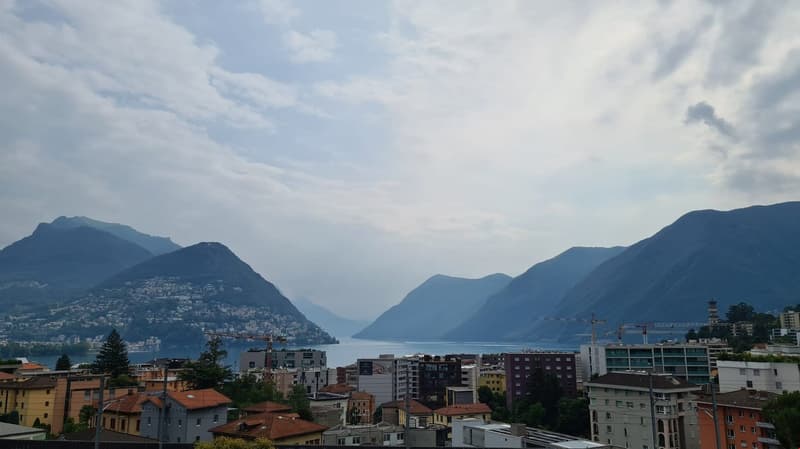 Wide panoramic view of mountainous region, water body, urban buildings, cranes, trees