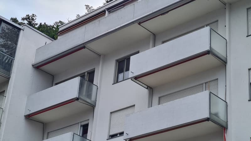 white building, multiple balconies with glass railings, several floors, window shutters