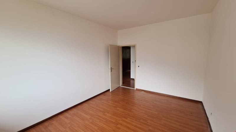 Empty room, wooden floor, white walls, open door leading to another room, power outlets on the wall