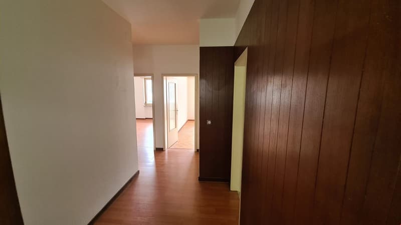 Empty hallway, wooden floors, white walls, wooden paneled wall, two open doors with windows and floor-to-ceiling doorways, hallway leads to two rooms.