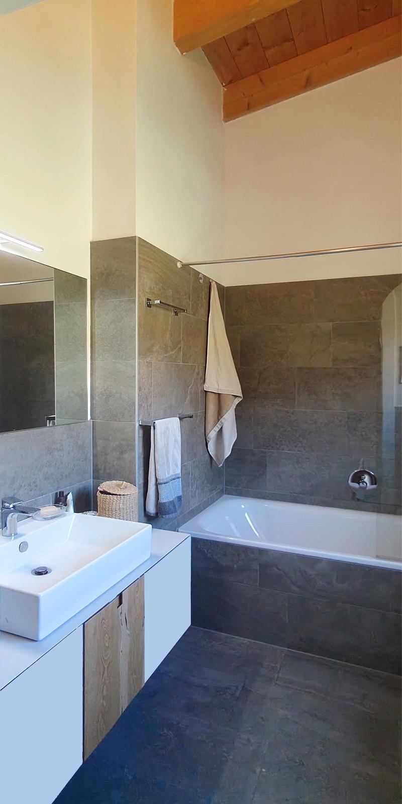 Bathroom with white sink, bathtub, mirror, wooden ceiling, towel racks, and tiled walls.