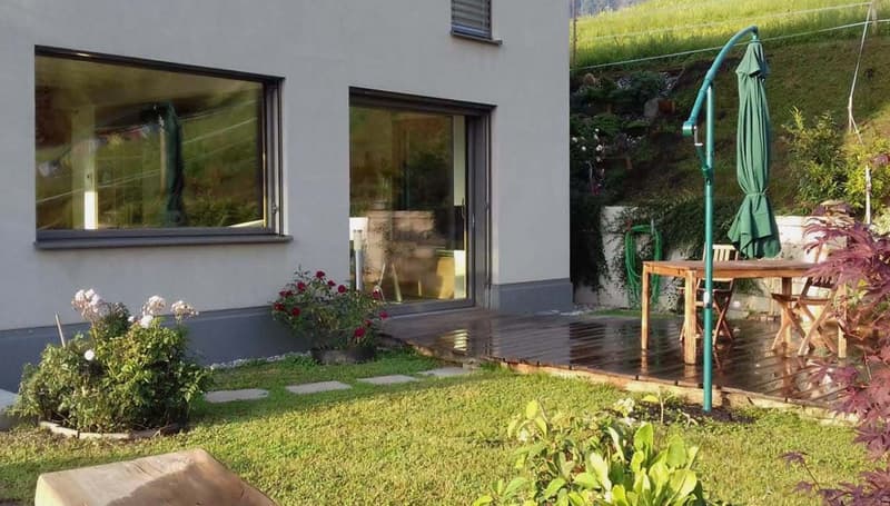 white exterior, large windows, wooden deck, outdoor table, green umbrella, garden, plants