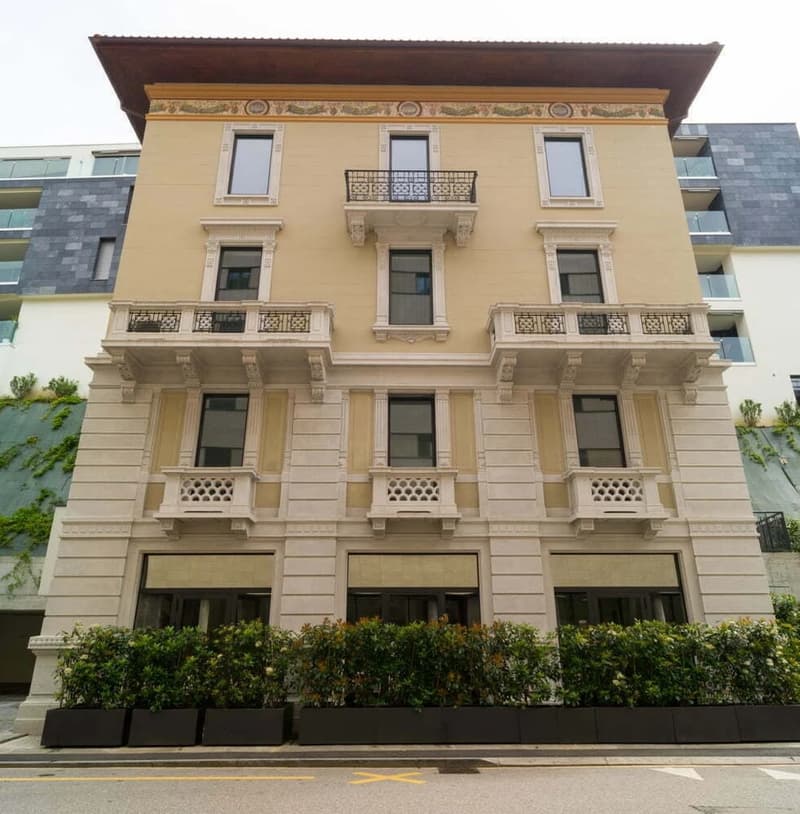 3 story building with beige paint, black iron balconies, window grills, greenery at the bottom