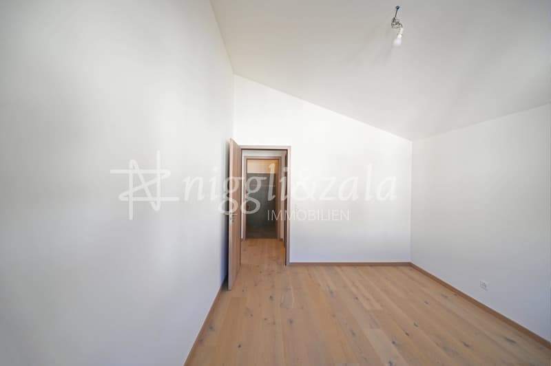 Empty room with wooden floor, white walls, open door leading to another room, ceiling light