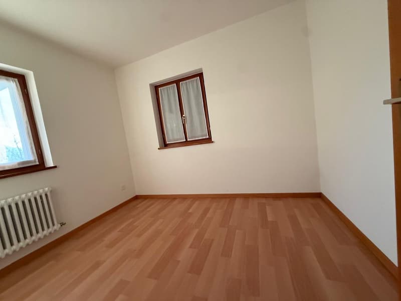 Empty room with wooden floors, white walls, windows, and a radiator.
