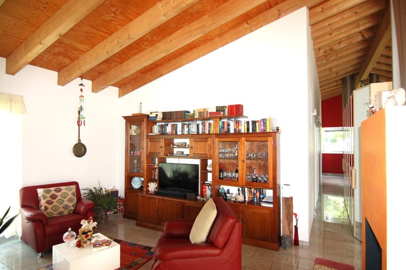 Spacious living room with wooden beamed ceiling, red leather sofas, wooden entertainment unit with TV, bookshelves, and decorative items