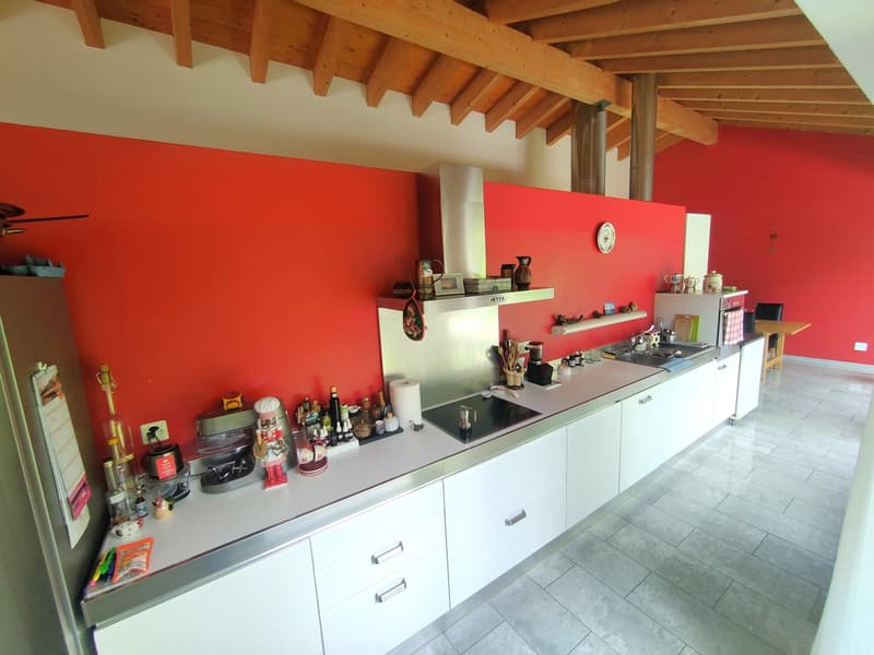 Spacious kitchen with red walls, wooden ceiling beams, white cabinets, stainless steel appliances, and various cooking utensils and supplies on the countertop.