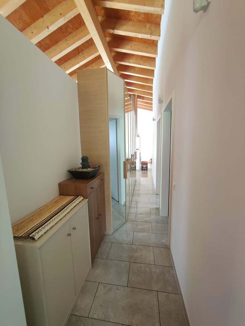 Wooden beamed ceiling, tiled floor, cabinet, and mirror in the hallway