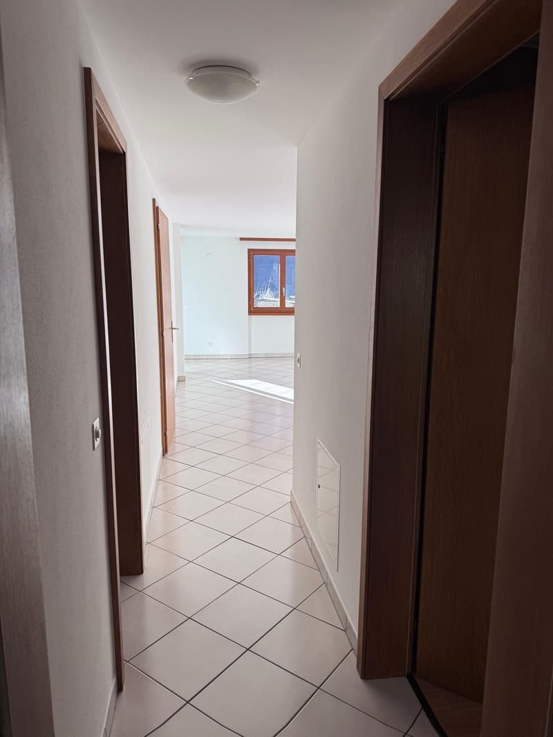 Long hallway, square tiles, white walls, ceiling light, windows with frames, doors on both sides