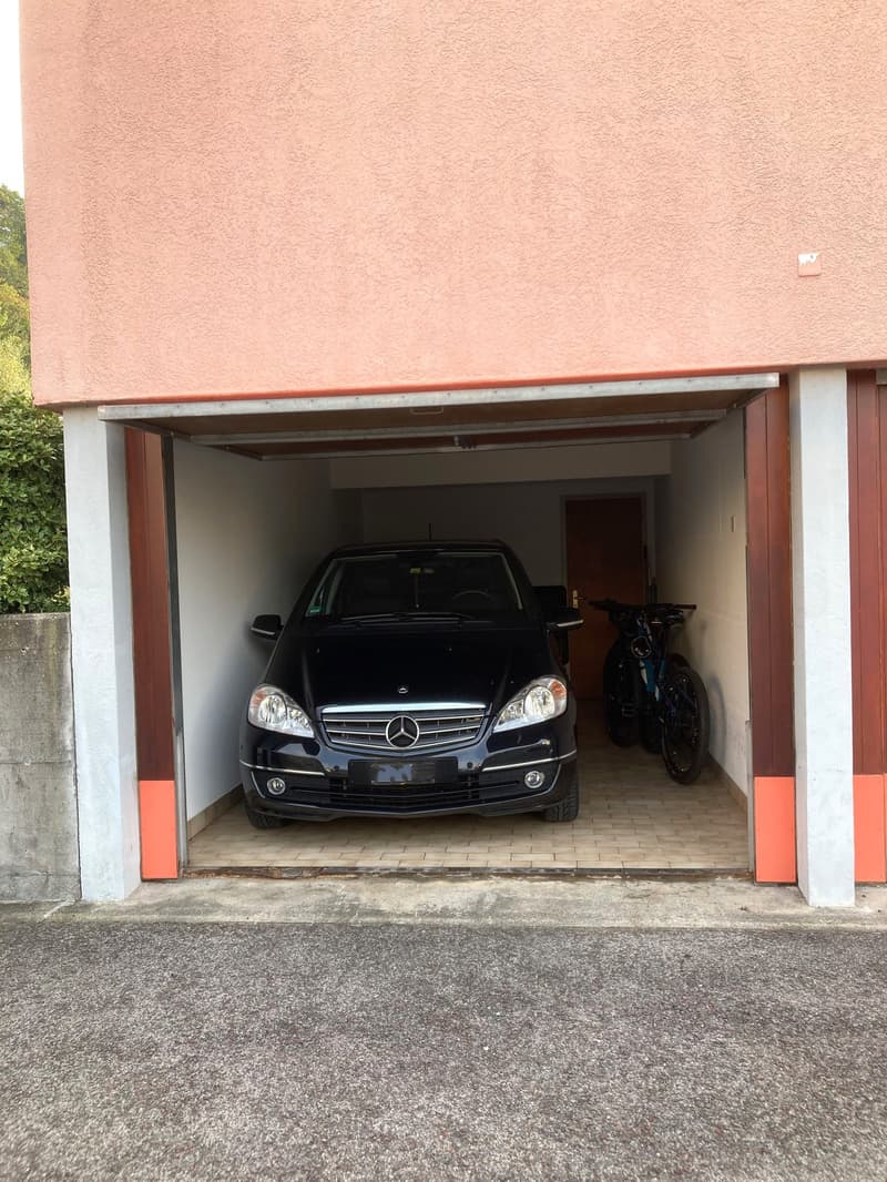 A car is parked in the garage with bicycles parked to the side